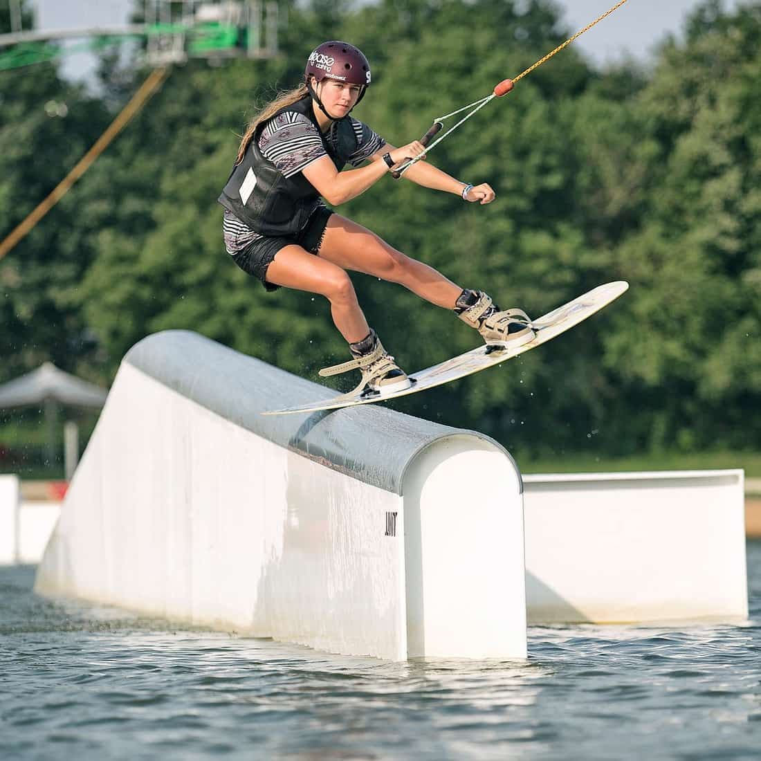 Wakeboarderin mit Helm und Weste fährt über eine Box an der Seilbahn